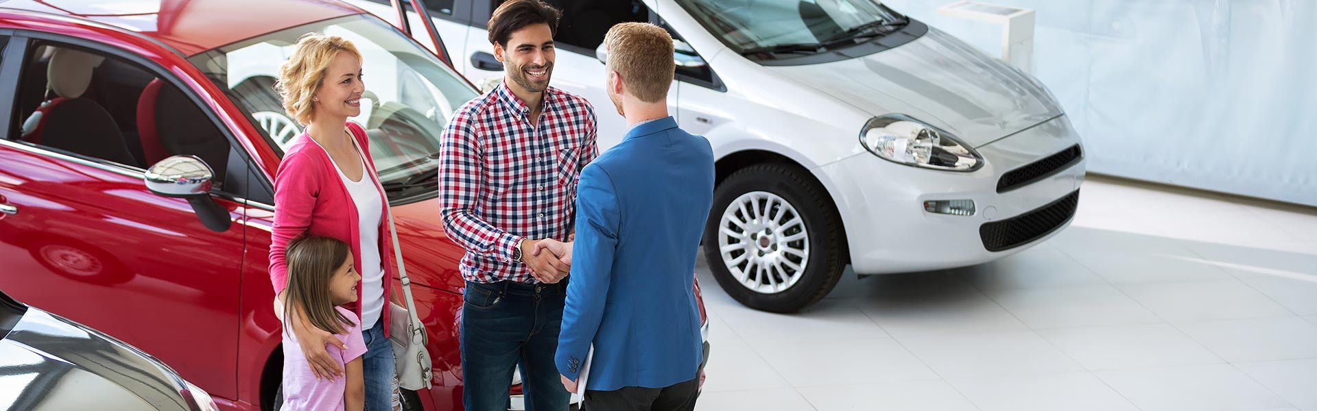 A man and woman pose in front of a car, both smiling and dressed casually.